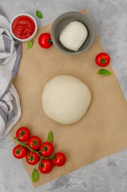 Fresh pizza dough with tomato sauce, mozzarella, tomatoes and basil leaves on a gray concrete background. Italian cuisine. Copy space