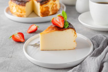 Bir parça Bask peynirli keki ya da San Sebastian peynirli keki gri arka planda beyaz bir tabakta taze çilek. Seçici odaklanma. Boşluğu kopyala