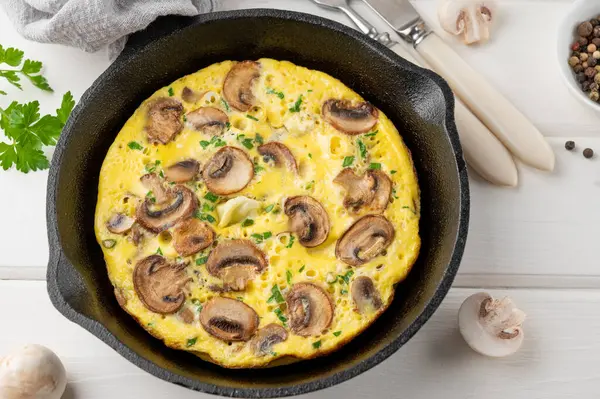 stock image Omelette with mushrooms and herbs in a pan on a white wooden background. Healthy breakfast. Top view. Copy space