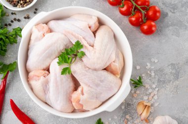 Taze otlu beyaz bir tabakta çiğ tavuk kanadı gri beton arka planda pişirmek için baharatlar. Üst görünüm, alanı kopyala