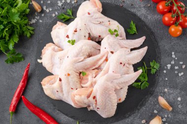 Çiğ tavuk kanatları ve taze otlar. Koyu beton zeminde pişirmek için baharatlar. Üst görünüm, alanı kopyala