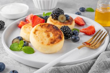 Süzme peynirli krep, şurup, taze böğürtlenli ricotta böreği, gri beton arka planda bal ve ekşi krema. Sağlıklı ve lezzetli bir kahvaltı. Üst görünüm, alanı kopyala