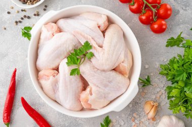 Taze otlu beyaz bir tabakta çiğ tavuk kanadı gri beton arka planda pişirmek için baharatlar. Üst görünüm, alanı kopyala