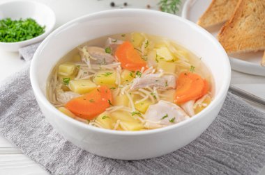 Erişteli tavuk çorbası ve ahşap arka planda beyaz kasede sebze.