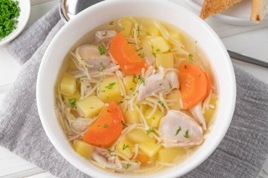 Chicken soup with noodles and vegetables in white bowl on a wooden background clipart