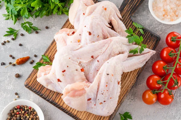 stock image Raw chicken wings on a wooden cutting board with spices, fresh herbs, tomatoes on a gray concrete background. Close up