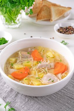 Erişteli tavuk çorbası ve ahşap arka planda beyaz kasede sebze.