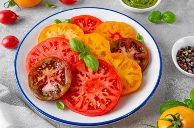 Gri beton arka planda pesto sosuyla dilimlenmiş sulu domates salatası. Yaz sağlıklı salata