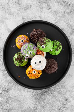 Ev yapımı komik canavar mini kekler ya da renkli çikolata jöleli ve şekerli kek parçaları. Beton zeminde Cadılar Bayramı hediyesi