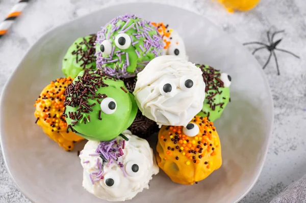 Homemade funny monster mini cakes or cake pops in a colored chocolate glaze and sugar sprinkles. Halloween treat on a concrete background