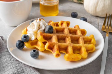 Baharatlı balkabaklı waffle, krema, bal ve yaban mersinli gri beton kaplama beyaz bir tabakta. Şükran Günü veya Cadılar Bayramı için tatlı