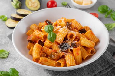 Norma usulü makarna. Patlıcanlı İtalyan makarnası, domates sosu, gri beton arka planda peynir ve fesleğen. Rahatlatıcı yemek.