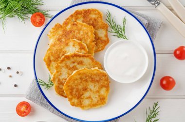 Patatesli gözleme, latke ya da taze otlu draniki ve beyaz ahşap arka planda bir tabakta ekşi krema. Üst görünüm, alanı kopyala