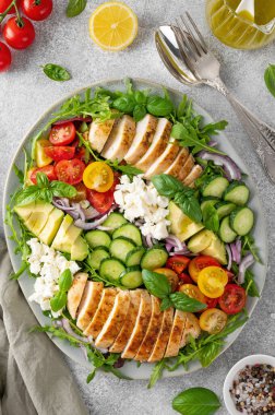 Kızarmış tavuklu salata, avokado, kiraz domatesleri, salatalık, roka peyniri ve gri beton kaplama bir tabakta. Sağlıklı yemek.