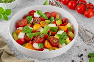 Kiraz domatesli Caprese salatası, mini mozzarella topları, avokado, pesto sosu ve taze fesleğen. Sağlıklı vejetaryen yemeği