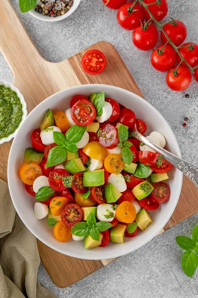 stock image Caprese salad with cherry tomatoes, mini mozzarella balls, avocado, pesto sauce and fresh basil. Healthy vegetarian meal