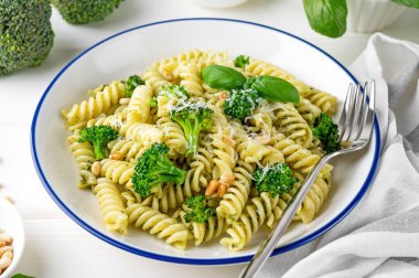 Pesto soslu vejetaryen makarna, brokoli, parmesan peyniri ve beyaz ahşap arka planda çam fıstığı. Sağlıklı yemek.