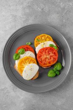 Çavdar ekmeği, domates, mozzarella ve çimento kaplı gri bir tabakta taze fesleğen. Sağlıklı yemek.