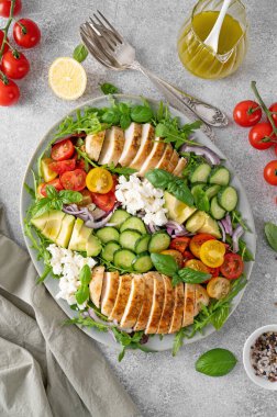 Kızarmış tavuklu salata, avokado, kiraz domatesleri, salatalık, roka peyniri ve gri beton kaplama bir tabakta. Sağlıklı yemek.