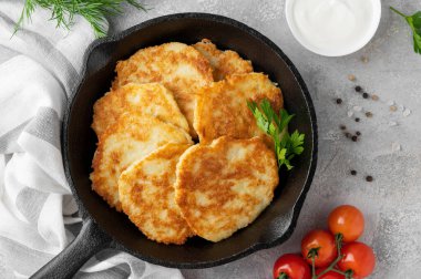 Patates gözlemesi, latke ya da taze otlu draniki ve gri beton arka planda dökme demir bir tavada ekşi krema. Üst görünüm, alanı kopyala