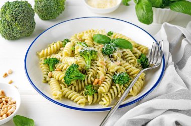 Pesto soslu vejetaryen makarna, brokoli, parmesan peyniri ve beyaz ahşap arka planda çam fıstığı. Sağlıklı yemek.