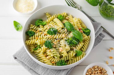 Pesto soslu vejetaryen makarna, brokoli, parmesan peyniri ve beyaz ahşap arka planda çam fıstığı. Sağlıklı yemek.