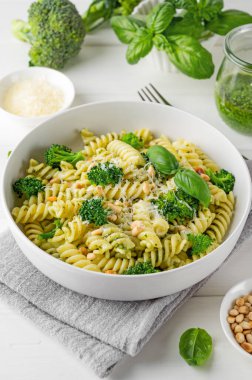 Pesto soslu vejetaryen makarna, brokoli, parmesan peyniri ve beyaz ahşap arka planda çam fıstığı. Sağlıklı yemek.