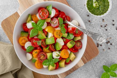 Caprese salad with cherry tomatoes, mini mozzarella balls, avocado, pesto sauce and fresh basil. Healthy vegetarian meal clipart