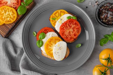 Çavdar ekmeği, domates, mozzarella ve çimento kaplı gri bir tabakta taze fesleğen. Sağlıklı yemek.