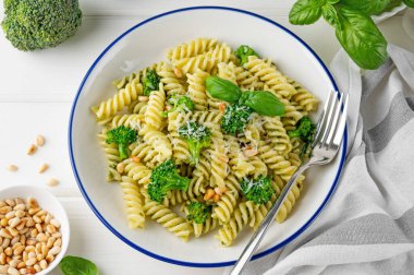 Pesto soslu vejetaryen makarna, brokoli, parmesan peyniri ve beyaz ahşap arka planda çam fıstığı. Sağlıklı yemek.