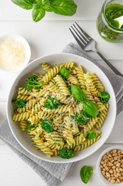 Pesto soslu vejetaryen makarna, brokoli, parmesan peyniri ve beyaz ahşap arka planda çam fıstığı. Sağlıklı yemek.