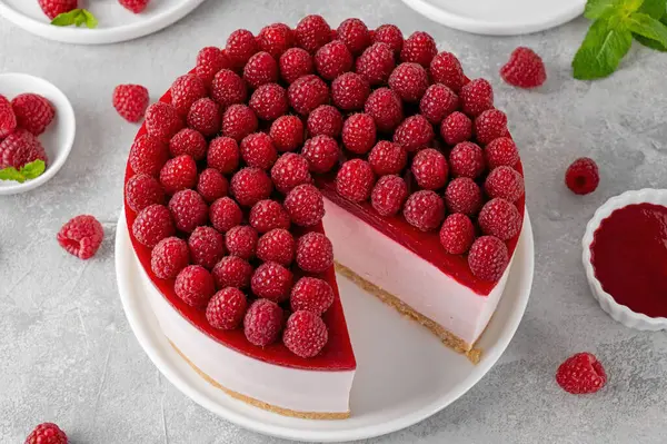 No baked raspberry cheesecake or raspberry cream mousse cake with jelly and fresh berries on top on a white plate on a gray concrete background. Summer cake
