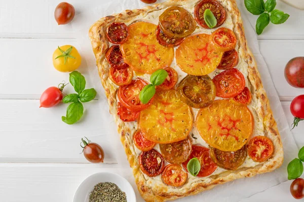 Tomatoes pie or galette from puff pastry and cheese filling on a white wooden background. Vegetarian healthy food. Selective focus