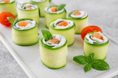 Salatalıklar krem peynirli rulo salatalık, tuzlu somon ve çimento zemin üzerinde beyaz seramik bir tahtada servis edilen taze otlar. Seçici odak.