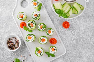 Salatalıklar krem peynirli rulo salatalık, tuzlu somon ve çimento zemin üzerinde beyaz seramik bir tahtada servis edilen taze otlar. Seçici odak.