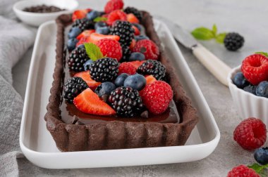 Taze böğürtlenli çikolatalı tart ve gri arka plandaki tabağın üstünde nane şekeri. Yaz tatlısı. Boşluğu kopyala