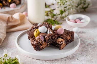 Chocolate brownie with Easter candies in the form of colored eggs with a bottle of milk. Easter dessert. Copy space clipart