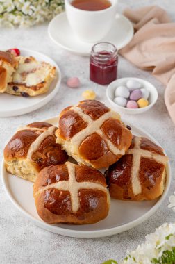 Geleneksel Paskalya çörekleri tereyağı, çilek reçeli ve bir fincan çayla birlikte beyaz bir tabakta. Lezzetli Paskalya kahvaltısı