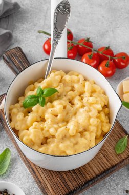 Beyaz bir tencerede makarna ve peynir, üzerinde taze fesleğen, tahta bir tahtanın üstünde gri beton bir arka planda. Amerikan mutfağı, rahat yemekler. Boşluğu kopyala