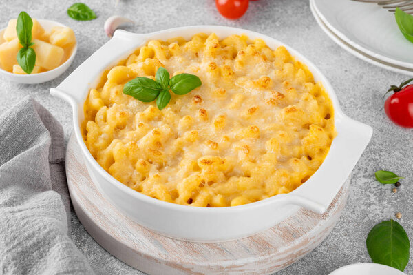 Мак и сыр в белой выпечке на деревянной доске на сером бетонном фоне. Американская кухня, еда для утешения. Копирование пространства