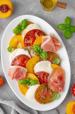 Dilimlenmiş çok renkli domates salatası, taze şeftali, mozzarella, prosciutto ve fesleğen. Lezzetli yaz salatası