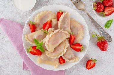 Lezzetli geleneksel hamur tatlısı, varenyky ya da çilekli pierogi ve beyaz tabakta ekşi krema.