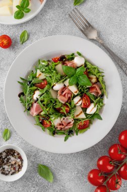 Taze yaz salatası roka, kavun, prosciutto ve mozzarella peyniri ile beton arka planda, sağlıklı yiyecekler. Üst görünüm