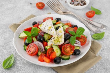 Yunan salatası taze meyve suyu, feta peyniri, otlar ve zeytinler beyaz bir tabakta açık beton arka planda. Sağlıklı yiyecekler. Boşluğu kopyala, üst görünüm