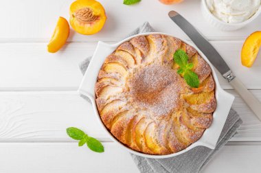 Beyaz ahşap zemin üzerinde beyaz seramik fırın şeklinde nefis şeftalili turta. Yaz pastası. Seçici odak, boşluğu kopyala