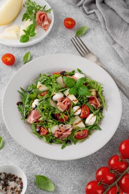 Taze yaz salatası roka, kavun, prosciutto ve mozzarella peyniri ile beton arka planda, sağlıklı yiyecekler. Üst görünüm