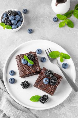 Çikolata kaplı brovniler, taze böğürtlenler ve nane yaprakları gri beton arka planda beyaz bir tabakta. Tatlı nefis.