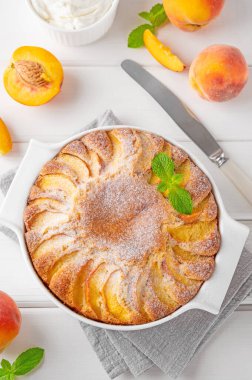 Beyaz ahşap zemin üzerinde beyaz seramik fırın şeklinde nefis şeftalili turta. Yaz pastası. Seçici odak, boşluğu kopyala