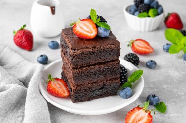 Çikolata kaplı bir yığın browni, gri beton arka planda beyaz bir tabakta taze böğürtlen ve nane yaprakları. Tatlı nefis.