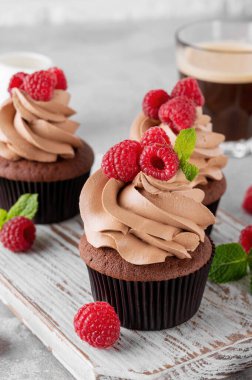 Kremalı çikolatalı kekler taze ahududu ve gri beton arka planda nane yapraklarıyla süslenmiş. Lezzetli bayram tatlısı.